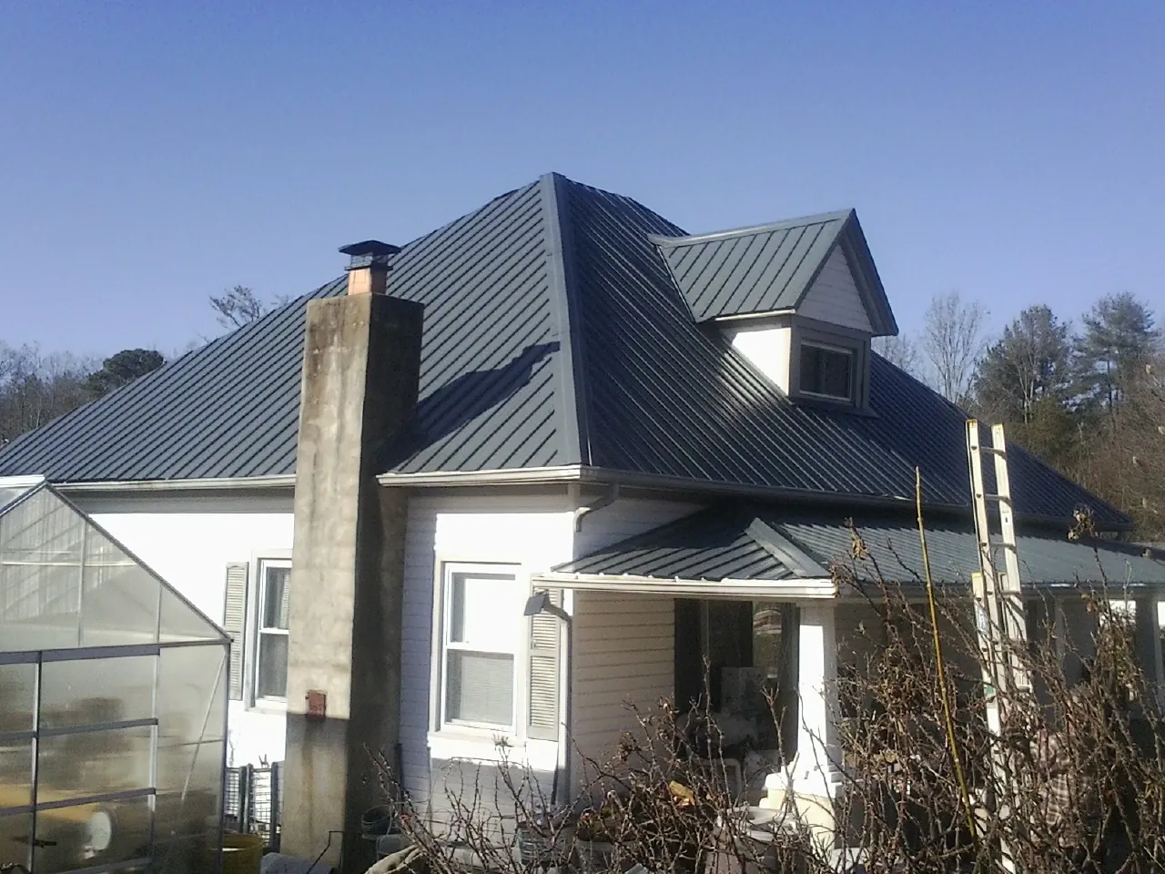 Dark blue standing seam metal roof on a white farmhouse with dormer — Slate & Tile Roof Repair by Roofing Brothers in Jacksboro