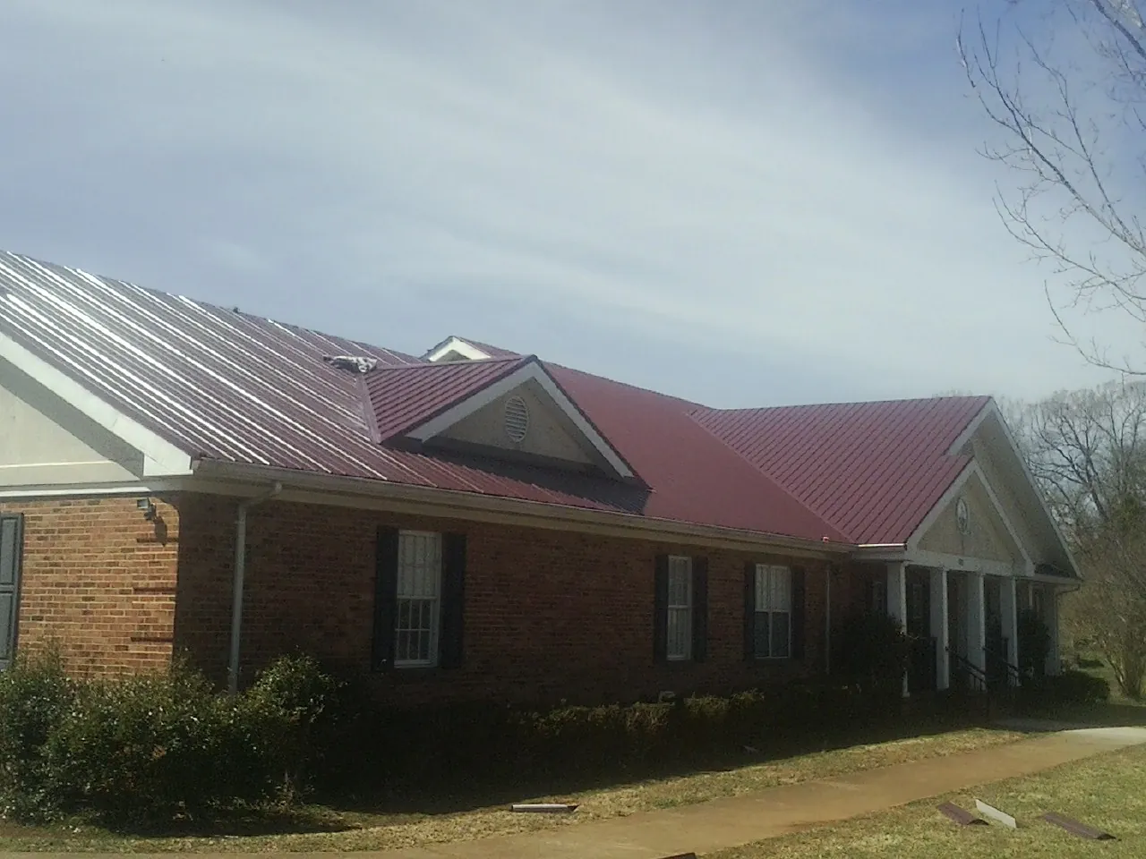 Red metal roof with gabled entries on a long brick building, from a Hail Damage Roof Repair job in Jacksboro