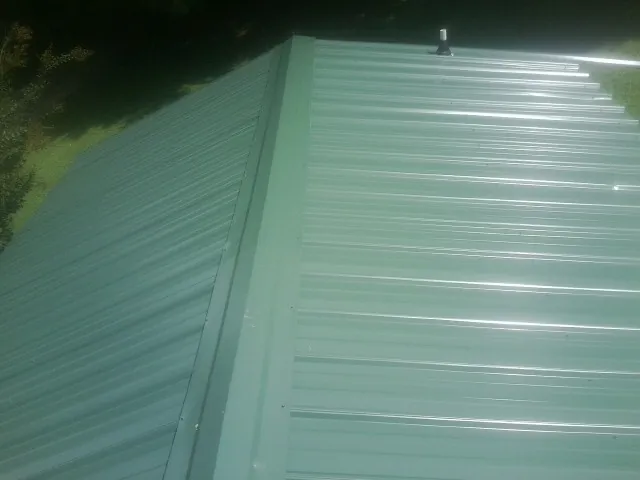 New green metal panels meeting at the ridge of a roof — Flat Roof Repair work by our crew in Jacksboro