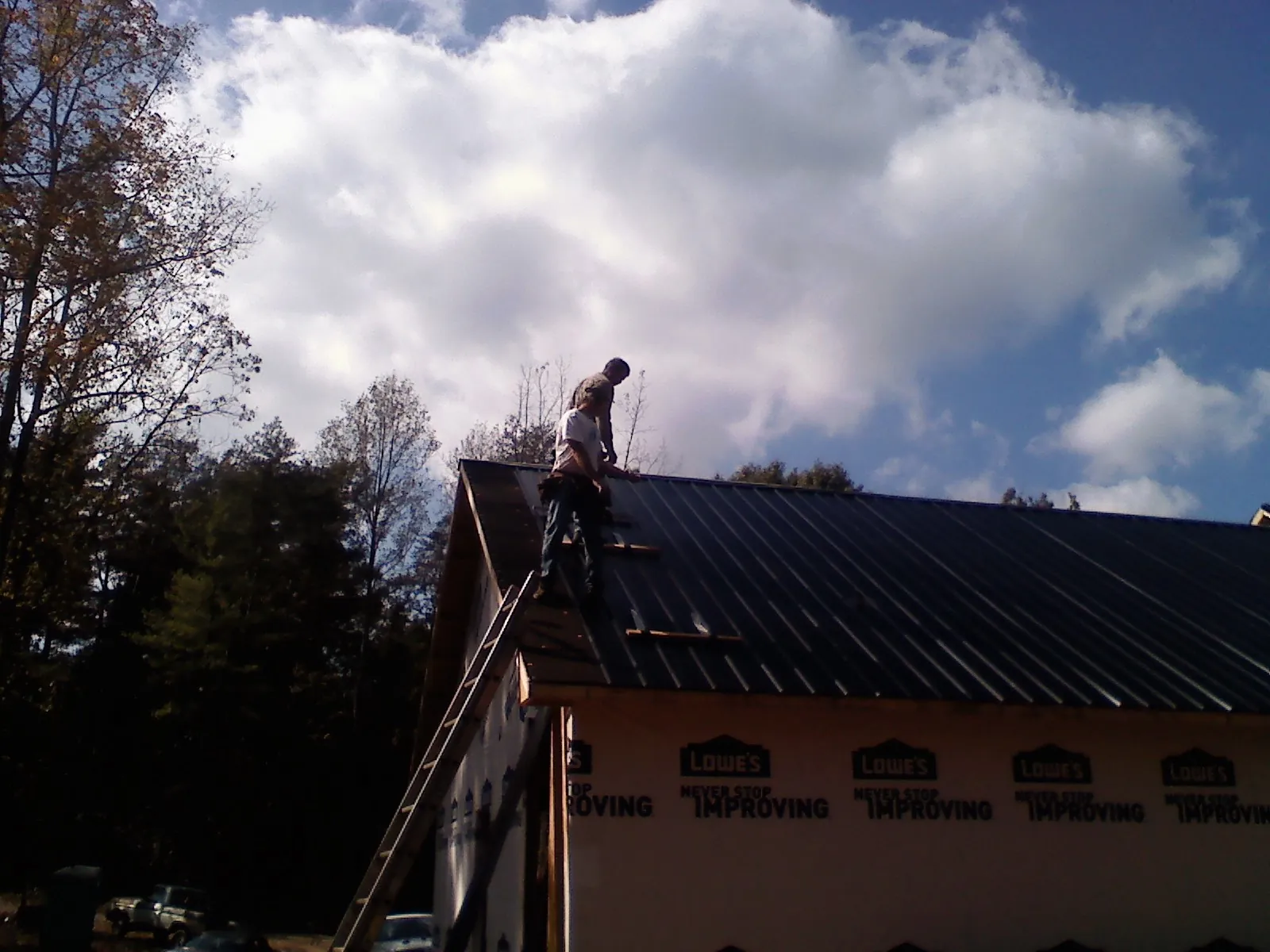 Roofer fastening dark metal panels high against a cloudy sky, from a Roof Inspection job in Jacksboro