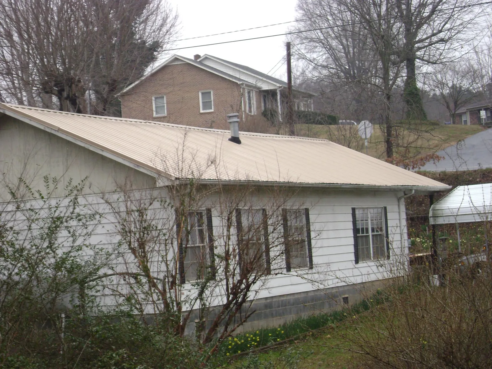 Tan metal roof on a white sided house set into a hillside — Commercial Roofing by Roofing Brothers in Jacksboro
