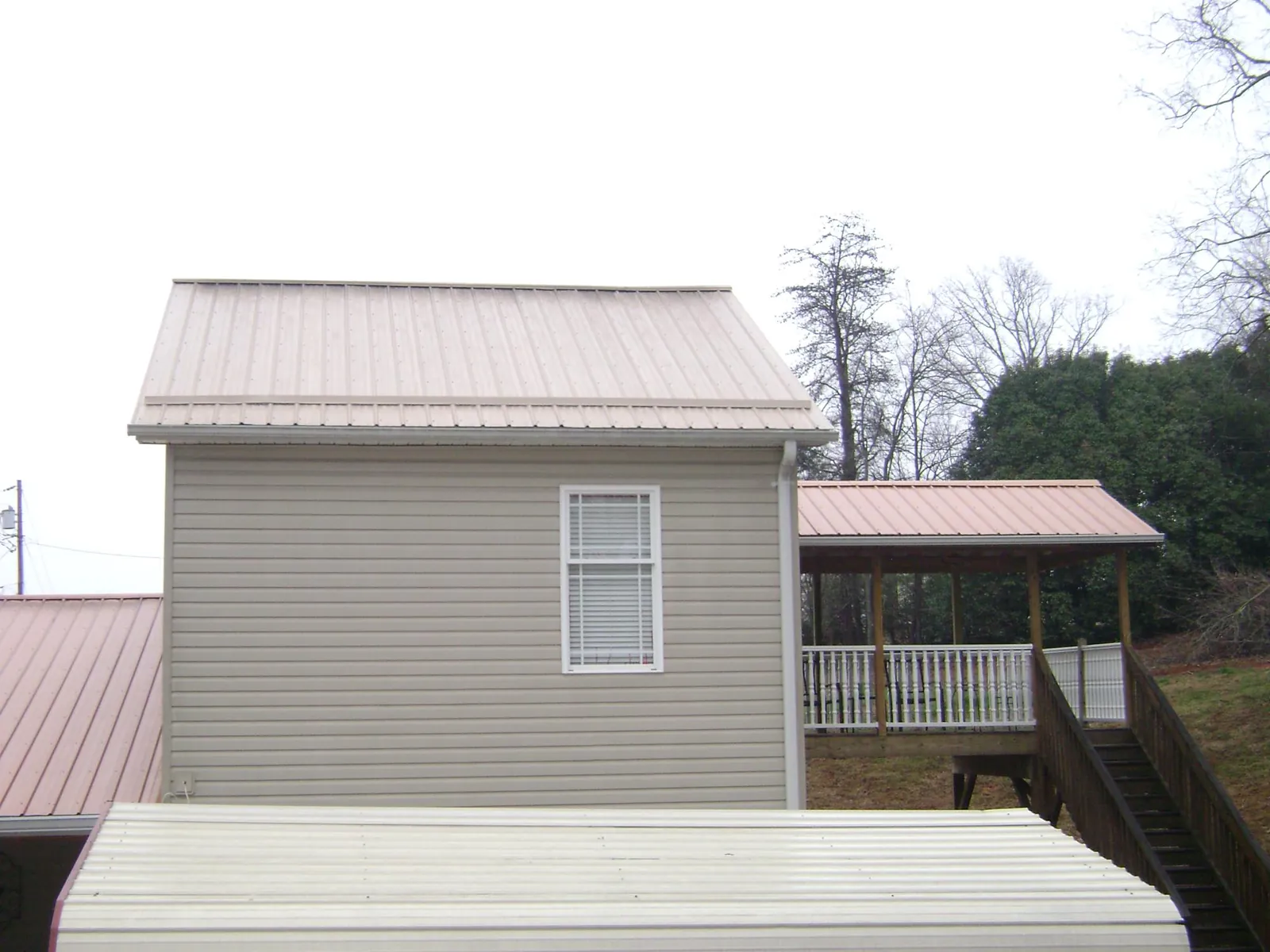 Tan metal roofs on a two story addition and attached porch, from a Roof Replacement job in Jacksboro